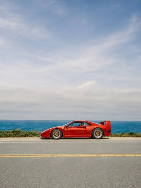 A red Ferrari F40 in profile beside the Pacific Ocean