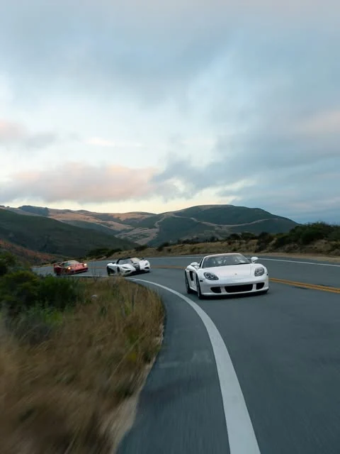 A Porsche Carrera GT leading the HIVE convoy through coastal hills