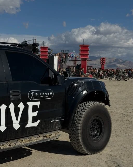 The black HIVE off-road truck at a dusty outdoor gathering